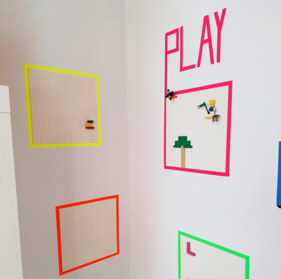Mehrere LEGO-Bauplatten mit farbigen Rahmen an einer Wand, darüber der Schriftzug PLAY.