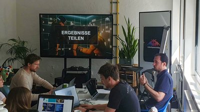 Bildschirm zeigt 'ERGEBNISSE TEILEN' während einer Präsentation von Tim Holmes im robotspaceship Workshop-Raum.