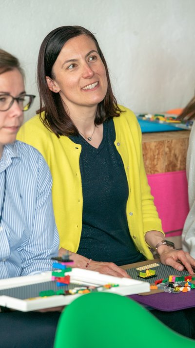 Lego Serious Play: Eine Frau schaut während einer Gruppenübung mit Lego-Bausteinen zu.