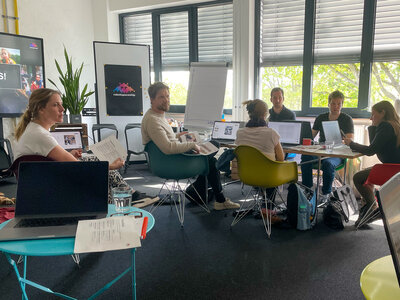 Workshop-Teilnehmer sitzen in einem hellen Raum, umgeben von Laptops und Präsentationsmaterial und tauschen sich über das Prompting in Adobe Firefly aus.