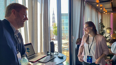 Aareon KI-Expedition in Mainz. Person spricht in ein Mikrofon mit KI-Voice-Agent Klara. Eine zweite Person hört zu und lacht.