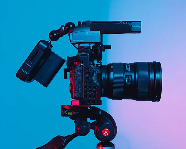 Professionelle Kamera auf Stativ in einem Studio, beleuchtet von blauem und rotem Licht.