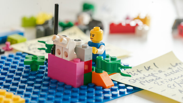 Lego Workshop: Nahaufnahme einer Lego-Figur und eines Modells mit Notizzetteln im Hintergrund.