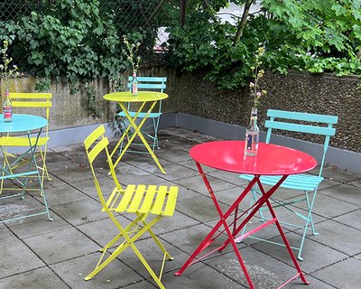 robotspaceship Terrasse mit bunten Gartentischen und Stühlen