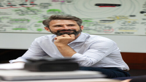 Porträt von Tom Klose mit weißem Hemd, der nachdenklich lächelt.