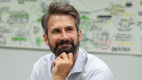 Porträt von Tom Klose mit weißem Hemd, der nachdenklich lächelt.